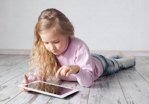 Child with tablet lying on floor. Girl playing laptop computer